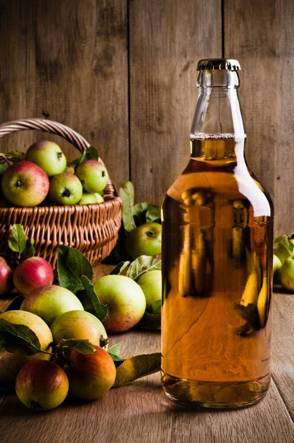 Фото: яблочное вино на фоне корзины с рассыпанными яблоками