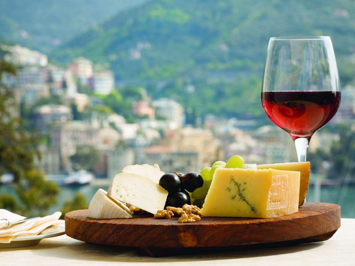 Фотография: итальянское красное вино на доске с сыром, орехами, оливками и виноградом на фоне классического провинциального итальянского города 