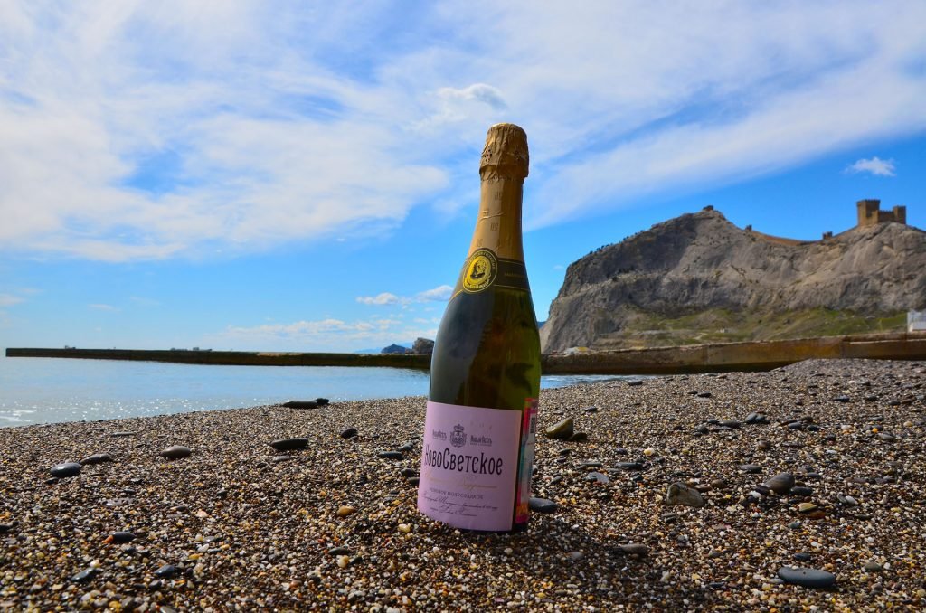 На фото бутылка с шампанским у берега моря на пляже. Крымские вина