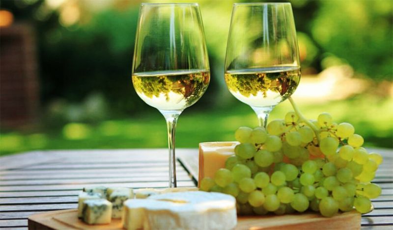 На картинке белое сладкое вино с кисточкой винограда на столе