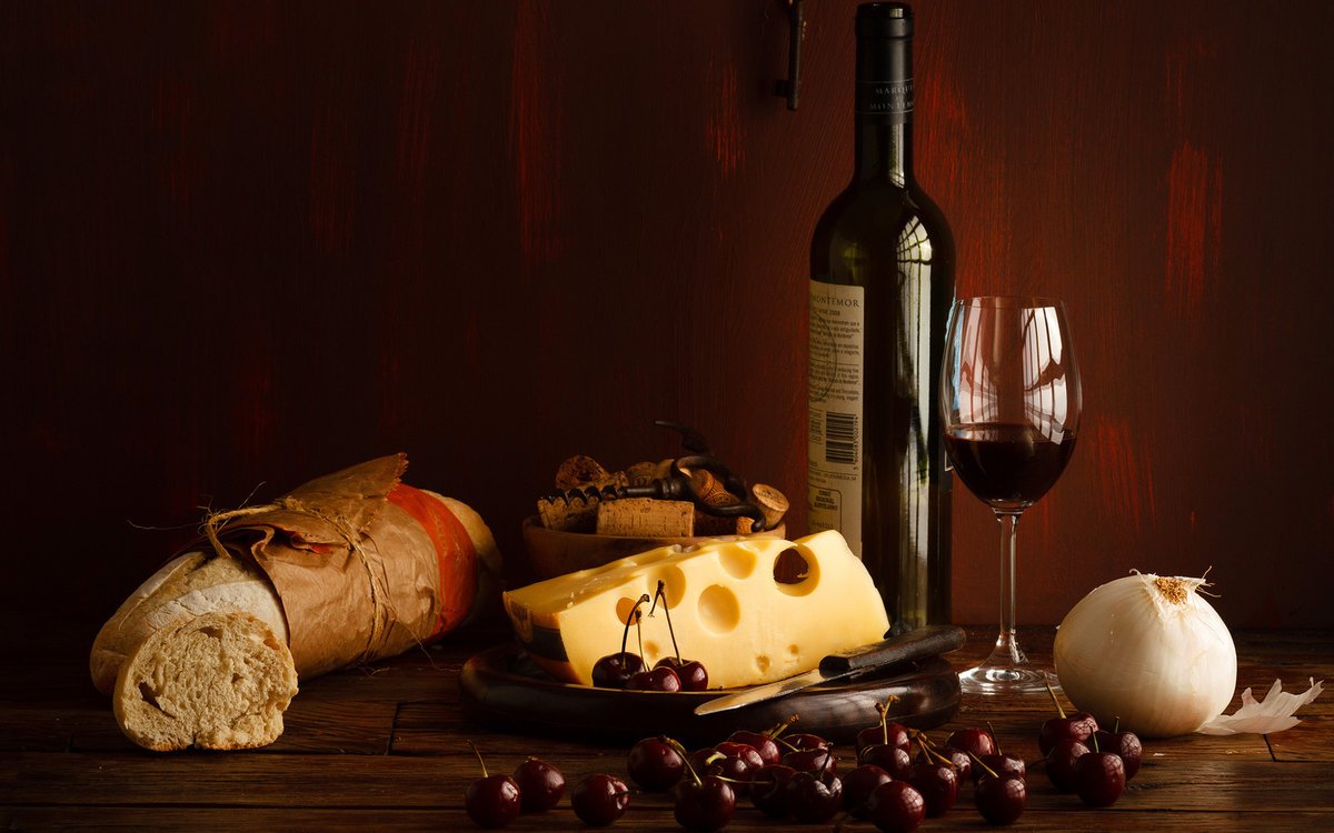 Винтажное фото бутылки вина, бокала, сыра, свежеиспеченного хлеба и ягод вишни на столе