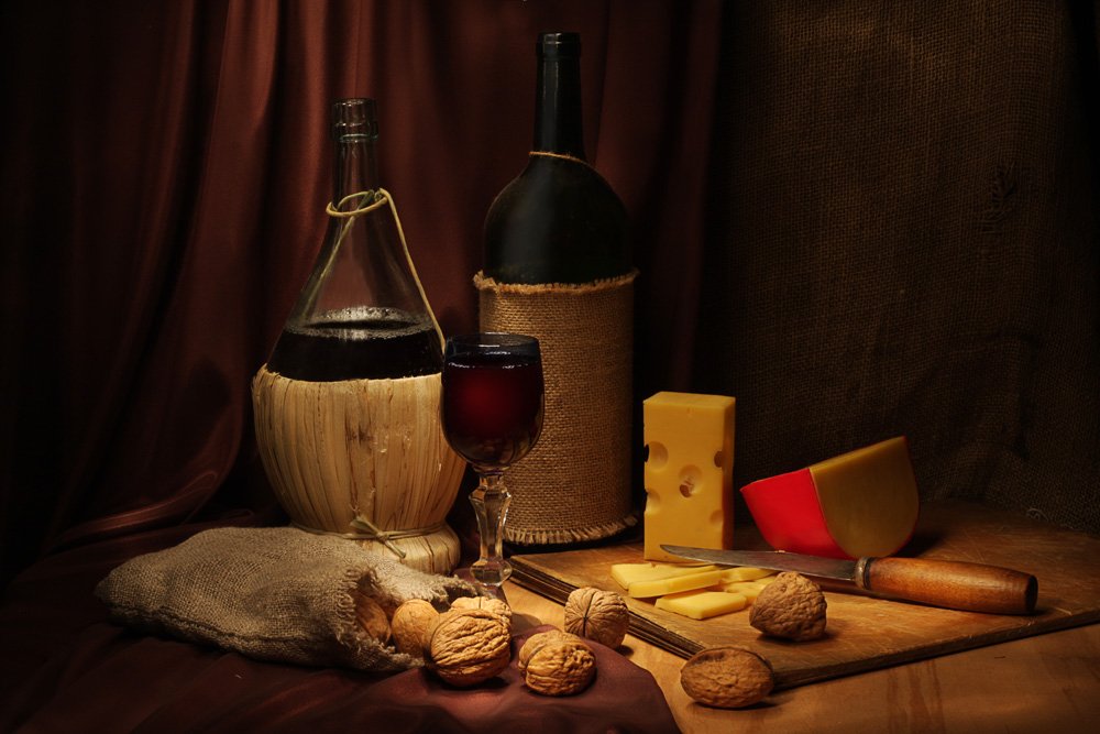 Натюрморт: бутылка красного вина, графин, бокал, сыр и орехи, высыпанные из мешочка